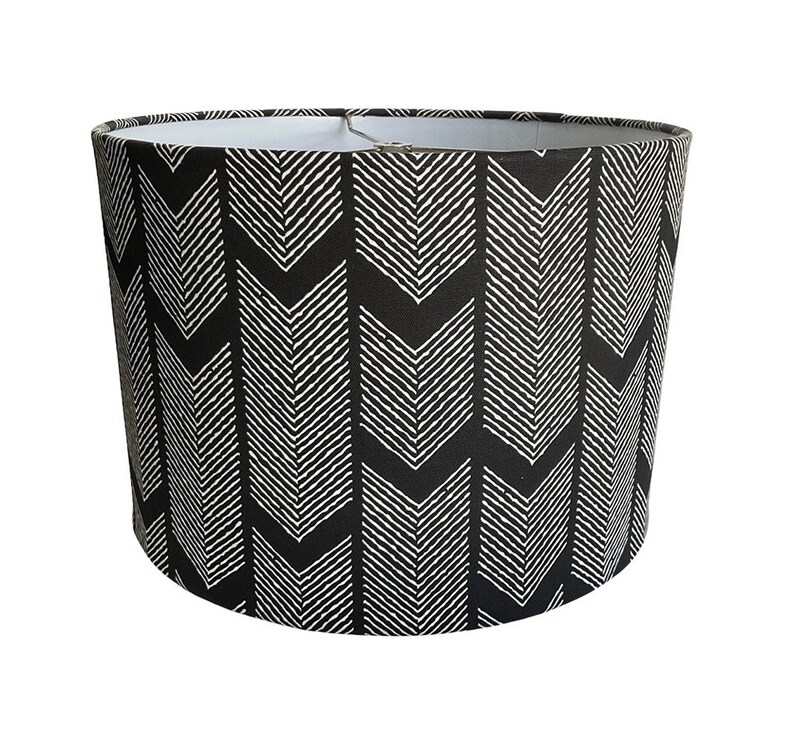 May include: Black and white lampshade with a chevron pattern. The lampshade is cylindrical and has a white interior.
