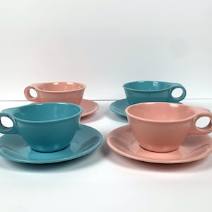 May include: Set of four teacups and saucers in pink and blue. The cups have a simple, rounded design and the saucers have a slightly flared edge.