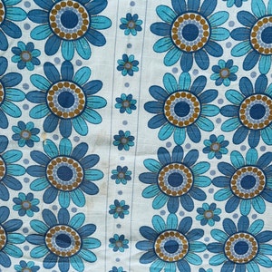 May include: A white fabric with a repeating pattern of blue and brown flowers. The flowers have a circular design in the center with a blue and brown ring around it.