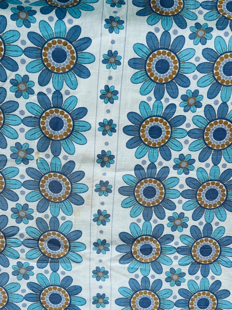 May include: A white fabric with a repeating pattern of blue and brown flowers. The flowers have a circular design in the center with a blue and brown ring around it.