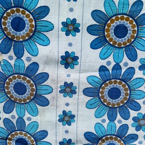 May include: White fabric with a repeating pattern of blue and brown flowers. The flowers have a circular center with a ring of brown dots around it.