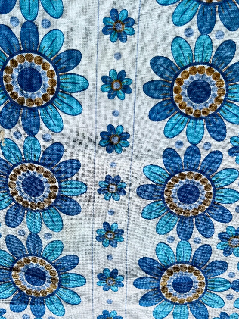 May include: White fabric with a repeating pattern of blue and brown flowers. The flowers have a circular center with a ring of brown dots around it.