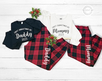 May include: Two pairs of red and black plaid pajama pants with white text. One pair says "Mommy 2023" and the other says "Daddy 2023".