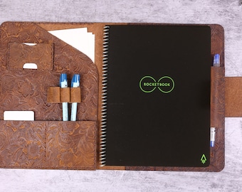 Könnte beinhalten: Ein braunes Leder-Rocketbook-Notizbuch mit schwarzem Einband und Spiralbindung. Das Notizbuch hat eine Tasche für Stifte und einen Kartensteckplatz. Der Einband hat ein geprägtes Blumenmuster.