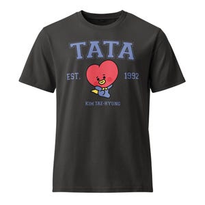 May include: Dark gray t-shirt featuring the word "TATA" in blue block letters above a red heart-shaped character with a yellow bow tie. The text "EST. 1992" and "KIM TAE-HYUNG" are also printed on the shirt.