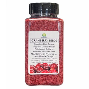 May include: A clear glass jar filled with red cranberry seeds. The label reads "CRANBERRY SEEDS" and lists the health benefits of the seeds, including complete plant protein, support for urinary health, and being a good source of fiber. The label also states that the seeds are heart healthy and contain omega 3. The jar is labeled with a net weight of 7 oz (203g).