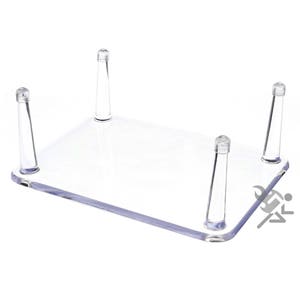 May include: A clear acrylic display stand with four legs. The stand is designed to hold small objects, such as figurines or collectibles.