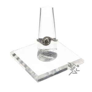 May include: A clear acrylic ring display stand with a single ring on it. The ring is a silver band with a large round center stone and smaller stones set around it.