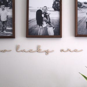 May include: Three black and white framed photos of families hanging on a white wall with the words "how lucky are we" in wooden letters underneath.