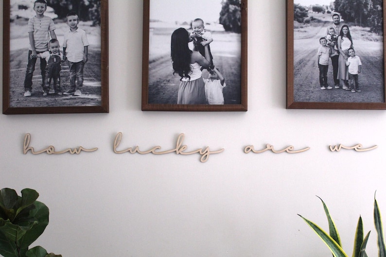 May include: Three black and white framed photos of families hanging on a white wall with the words "how lucky are we" in wooden letters underneath.