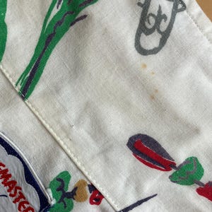 May include: Close-up of a white fabric with a repeating pattern of green, purple, red, and gray illustrations. The fabric has a stitched seam and a blue and white patch with the word "MASTER".
