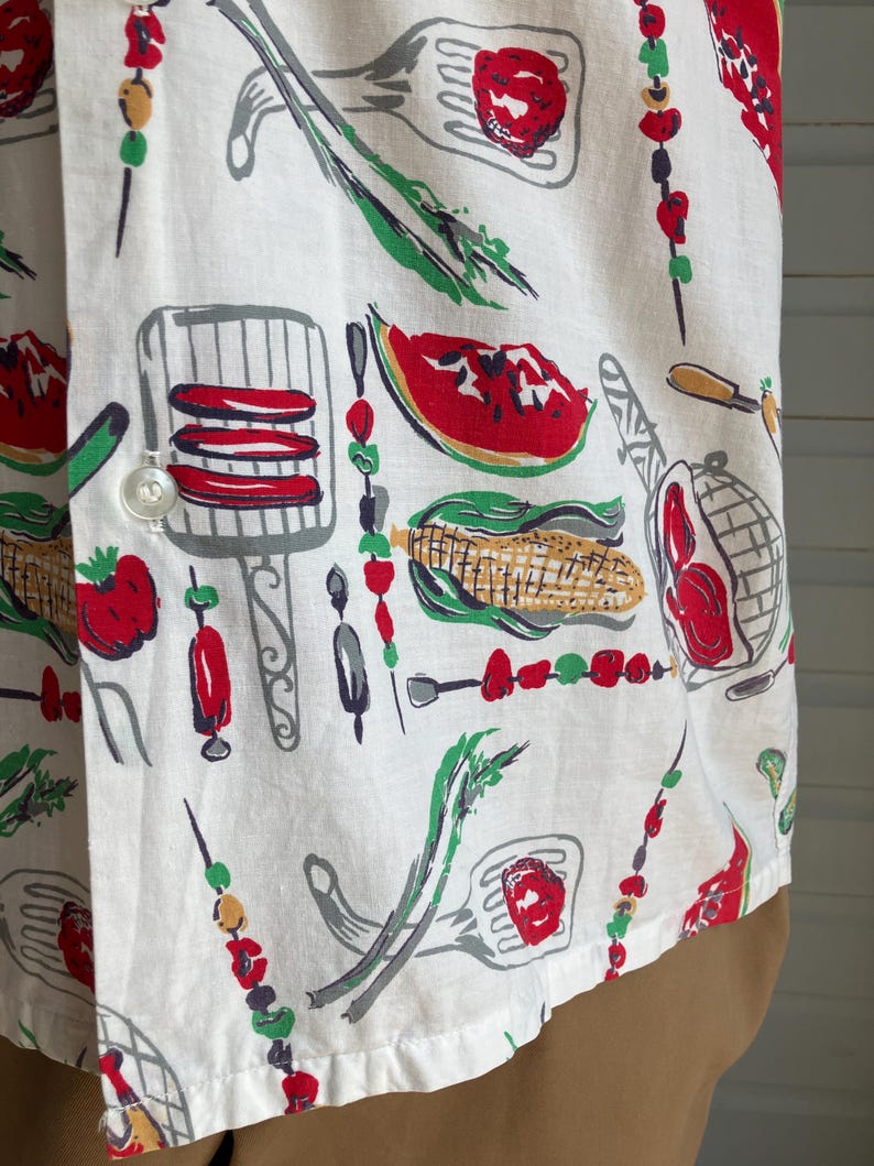 May include: White button-down shirt with a colorful barbecue-themed print. The pattern includes illustrations of grilled food, skewers, watermelon slices, and grilling utensils in red, green, and gray.