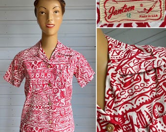 Pode incluir: Uma camisa vintage de manga curta com padrão vermelho e branco com botões de madeira. A camisa apresenta um design único de inspiração tribal. A etiqueta diz "Jantzen 12 Made in U.S.A."