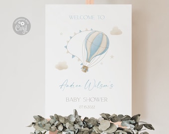 May include: Welcome to Andrea Wilson's Baby Shower sign featuring a blue and white hot air balloon illustration. The sign is displayed on a wooden easel.
