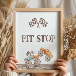 May include: A wooden sign with the text "PIT STOP" in brown lettering. The sign features a checkered flag and two cartoon monster trucks on a gray road.