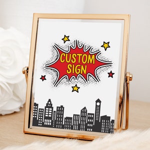 May include: A gold-coloured picture frame with a white background and a red and yellow comic book style speech bubble that says "CUSTOM SIGN". The speech bubble is over a black silhouette of a city skyline.