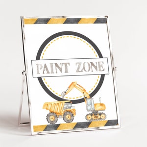 Puede incluir: Un cartel imprimible con un borde rayado negro y amarillo. El cartel tiene un círculo negro con un círculo punteado amarillo en su interior. El texto "PAINT ZONE" está en el centro del círculo. Hay dos vehículos de construcción amarillos, un camión volquete y una excavadora, en la parte inferior del cartel.