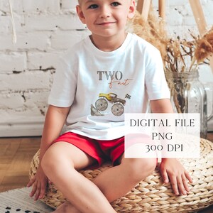May include: A young child wearing a white t-shirt with a monster truck graphic and the text "TWO fast" printed on it. The child is sitting on a woven basket.