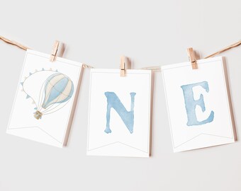 May include: A blue and white hot air balloon with a banner that says "ONE" in blue watercolor letters. The banner is strung with twine and clothespins.