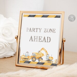 Może przedstawiać: Złoty znak z białym tłem i czarno-żółtą paskowaną ramką. Na znaku widnieje napis "Party Zone Ahead" srebrnymi literami. Są ilustracje pojazdów budowlanych, w tym żółtej wywrotki i żółtej koparki.