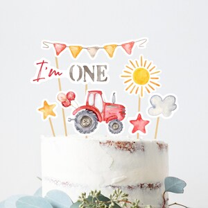 May include: Red tractor cake topper with balloons, a sun, a cloud, and two stars. The topper also includes a banner that says "I'm ONE".