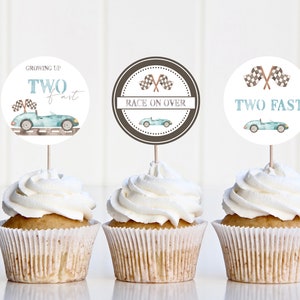 May include: Three cupcake toppers with a racing car theme. The toppers are round and white with blue and brown accents. The text on the toppers reads "Growing Up Two Fast", "Race On Over", and "Two Fast".
