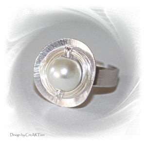 Könnte beinhalten: Ein silberner Ring mit einer weißen Perle, die in einem Drahtkäfig-Design eingefasst ist.