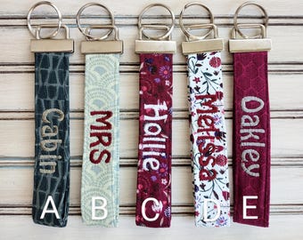 May include: Five keychains with different fabric patterns and personalized names. The names are Cabin, Mrs, Hollie, Melissa, and Oakley. The keychains are labeled A through E.