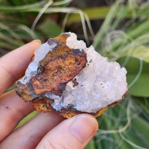 May include: A cluster of white quartz crystals with a brown and orange iron oxide matrix. The crystals are translucent and have a glassy luster.