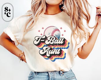 May include: A white t-shirt with a retro-style graphic of a baseball and the text "T-Ball Aunt".