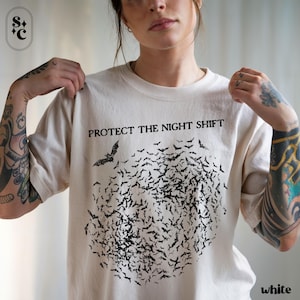May include: Cream-colored t-shirt with the text "PROTECT THE NIGHT SHIFT" above a flock of black bats. The bats form a circular shape. The word "white" is printed at the bottom right.
