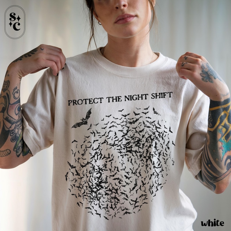 May include: Cream-colored t-shirt with the text "PROTECT THE NIGHT SHIFT" above a flock of black bats. The bats form a circular shape. The word "white" is printed at the bottom right.
