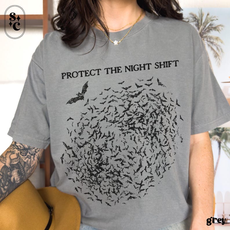 May include: A grey t-shirt with the text "PROTECT THE NIGHT SHIFT" above a graphic of a bat and a swarm of bats. The shirt is a solid grey color.