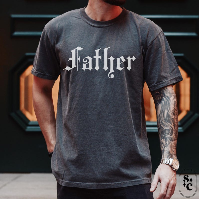 May include: A dark gray t-shirt with the word "Father" printed in white in a gothic font.
