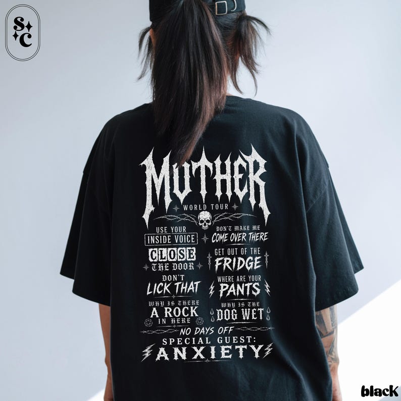 May include: A black short-sleeved t-shirt featuring white graphic text on the back. The design includes the word MUTHER, WORLD TOUR, and phrases like USE YOUR INSIDE VOICE, CLOSE THE DOOR, DON'T LICK THAT, GET OUT OF THE FRIDGE, and ANXIETY.