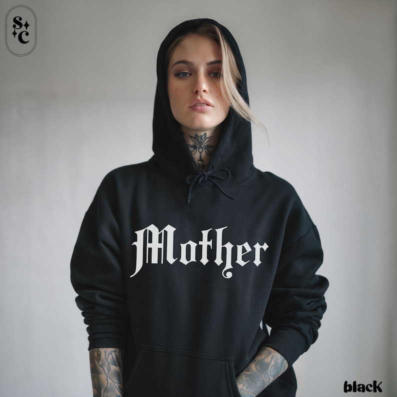 May include: Black hooded sweatshirt with the word "Mother" in a gothic font across the chest. The sweatshirt has a drawstring hood and a front pocket. The word "black" is in the bottom right corner.