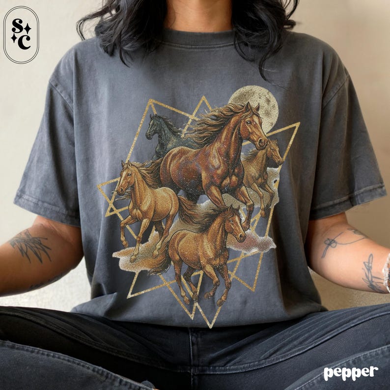May include: Dark grey t-shirt with a graphic of running horses in brown and tan, set against a gold geometric design and a full moon. The shirt has a vintage, worn appearance.