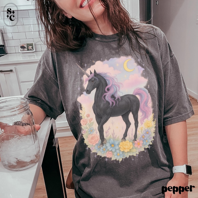 Peut inclure: T-shirt gris fonc&eacute; avec un motif de licorne noire, crini&egrave;re et queue violettes et roses. La licorne est entour&eacute;e de fleurs et d'un croissant de lune. Le mot "pepper" est imprim&eacute; en bas &agrave; droite.