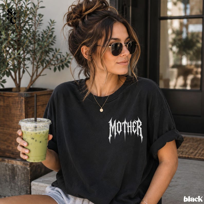 May include: A black short-sleeved t-shirt featuring the word MOTHER printed in a white, jagged, metal-style font on the left chest area. The shirt has a crew neckline and a relaxed fit, made from a solid black fabric with a matte finish.