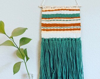 Puede incluir: Un tapiz tejido para colgar en la pared con un patrón de rayas verdes, blancas y marrones y flecos verdes.