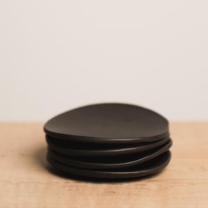 May include: A stack of five black ceramic saucers. The saucers are round and have a slightly uneven edge.