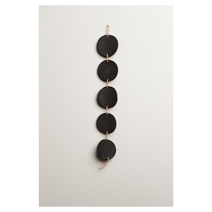 Puede incluir: Una decoración de pared de cerámica negra con cinco discos redondos conectados por un cordón marrón.