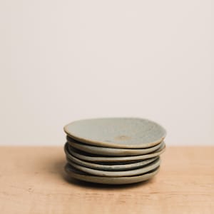 Puede incluir: Una pila de siete platos pequeños, redondos, de cerámica azul claro con una superficie texturizada.