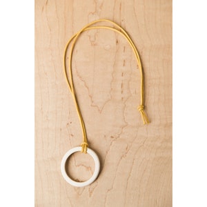 May include: A white ceramic ring pendant on a yellow cord necklace.