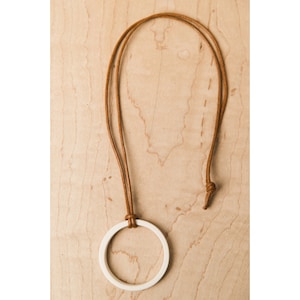 May include: A white ceramic circle pendant on a brown leather cord necklace.