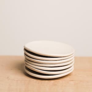 May include: A stack of eight off-white ceramic saucer-shaped dishes.
