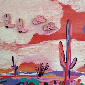 May include: Pink cowboy boots and hats with gold accents on a colorful desert landscape background.
