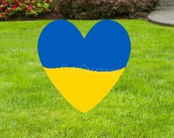 May include: A heart-shaped lawn decoration in the colors of the Ukrainian flag. The heart is blue on top and yellow on the bottom. The heart is on a green lawn in front of a house.