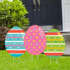 May include: Three large Easter egg yard decorations. The eggs are pink with white polka dots, blue with white stripes and red zigzags, and green with yellow stripes and red zigzags.