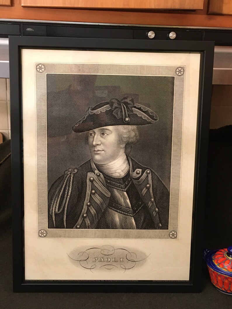 May include: A black and white portrait of a man in a military uniform wearing a tri-cornered hat. The portrait is framed in a black frame and has a decorative border with stars. The name "PAOLI" is written in a decorative script below the portrait.